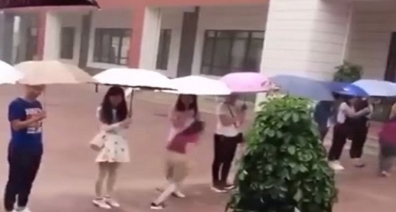 بالفيديو.. معلمون يقفون بمظلاتهم لينتقل الطلاب من مبنى لآخر