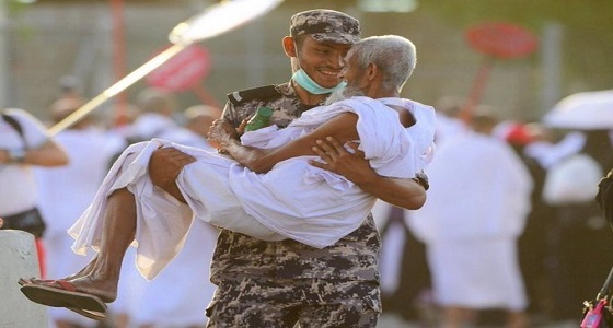 رجل أمن مبتسم يحمل حاجا مسنا داخل المشاعر المقدسة أثناء أداء مناسك الحج