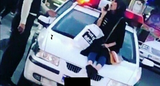 « إيرانية » تخلع حجابها وتجلس على سيارة للشرطة للاحتجاج