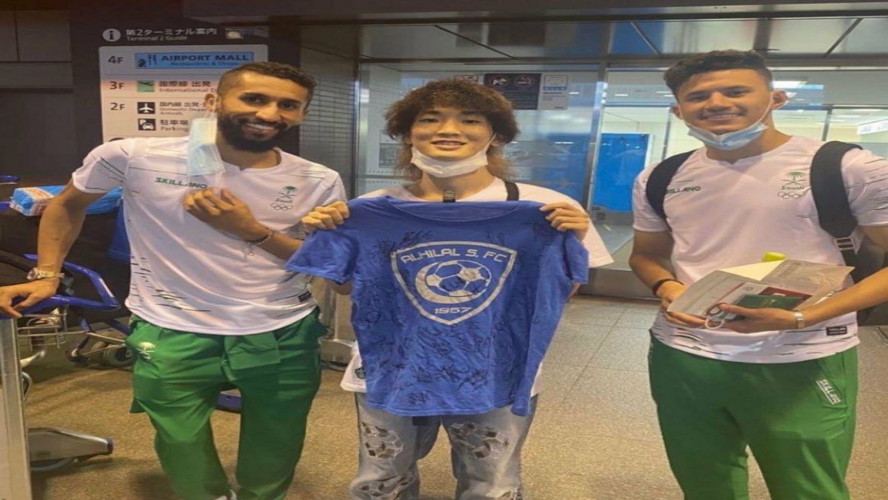 مشجع ياباني يحمل شعار الهلال أثناء استقباله الأخضر الأولمبي ويلتقط صورة مع الفرج والحمدان