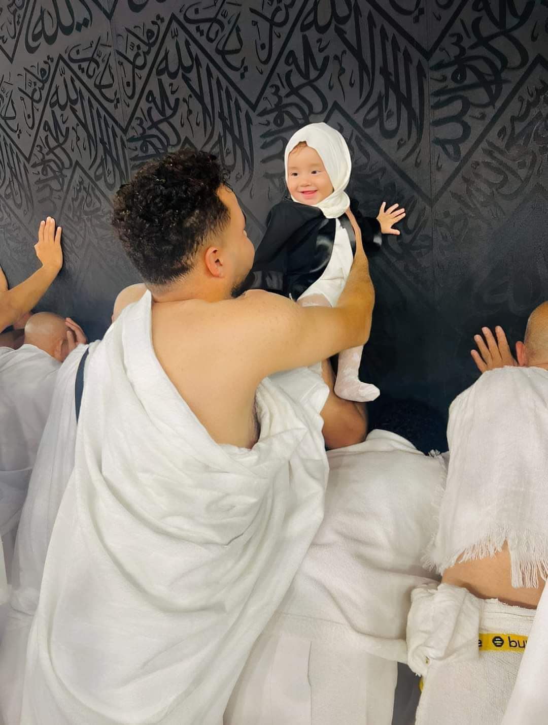 صورة مؤثرة لطفلة رضيعة تبتسم لوالدها أثناء لمسها الكعبة الشريفة