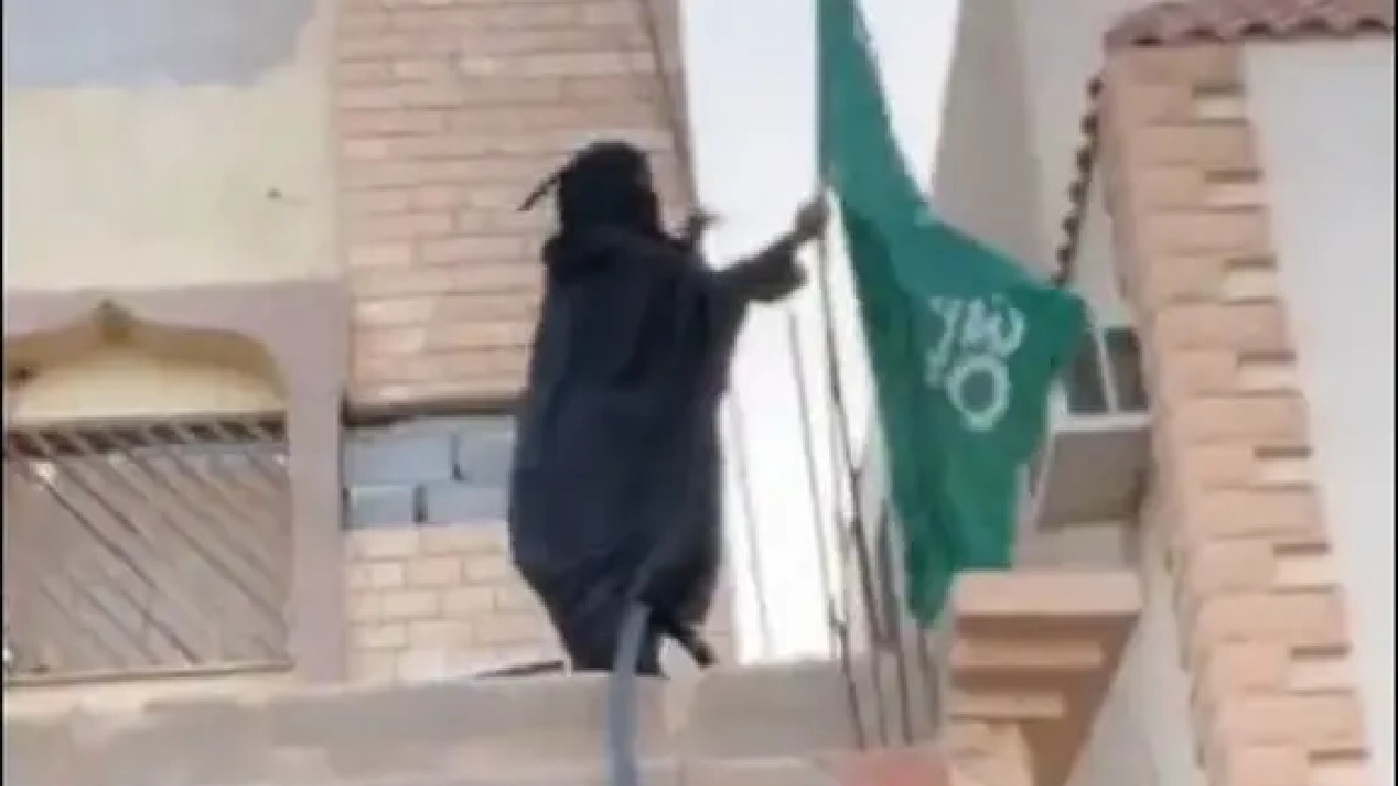 شاهد.. مواطنة مسنة تصعد على سور منزلها لترفع العلم السعودي